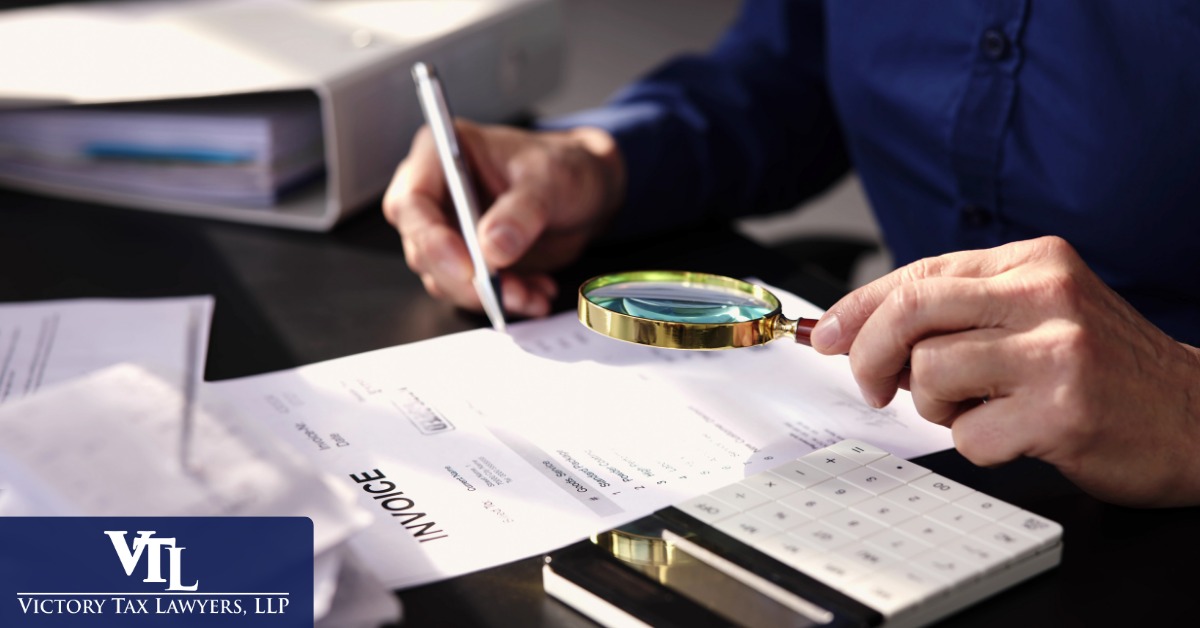 Auditor examining an invoice through a magnifying glass beside a calculator and files
